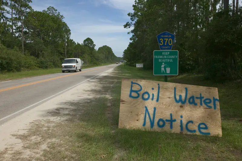 A hand-painted Boil Water Notice sign standing beside a rural Gulf Coast road
