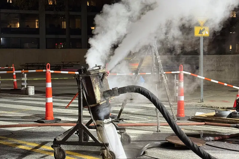 Steam drifting out of an open manhole while a cured-in-place liner hardens inside the sewer pipe below