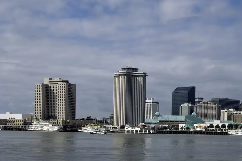 Downtown New Orleans towers seen across the Mississippi River under a cloudy sky, with riverboats moored along the bank