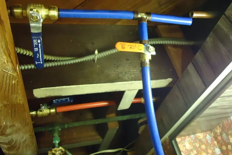 Blue and red PEX supply lines with brass quarter-turn shut-off valves running along wooden floor joists