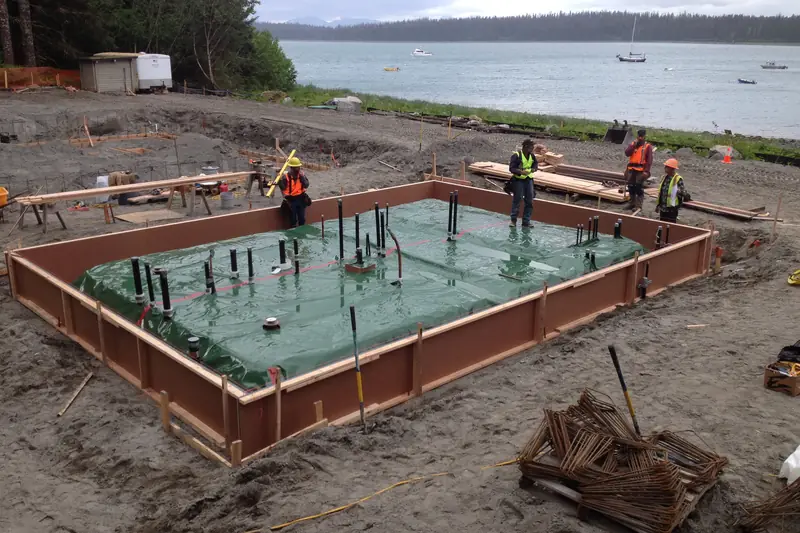 Wooden slab formwork over a green vapor barrier, with black plumbing pipes rising through it before the concrete pour